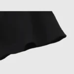 Close-up of a black fabric edge from a Hellstar Path To Paradise T-shirt against a light gray background, highlighting the texture and stitching detail of the material.